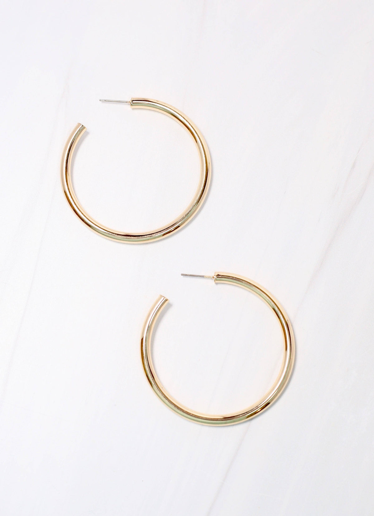 Pair of large gold tubular hoop earrings with post backs on marble surface