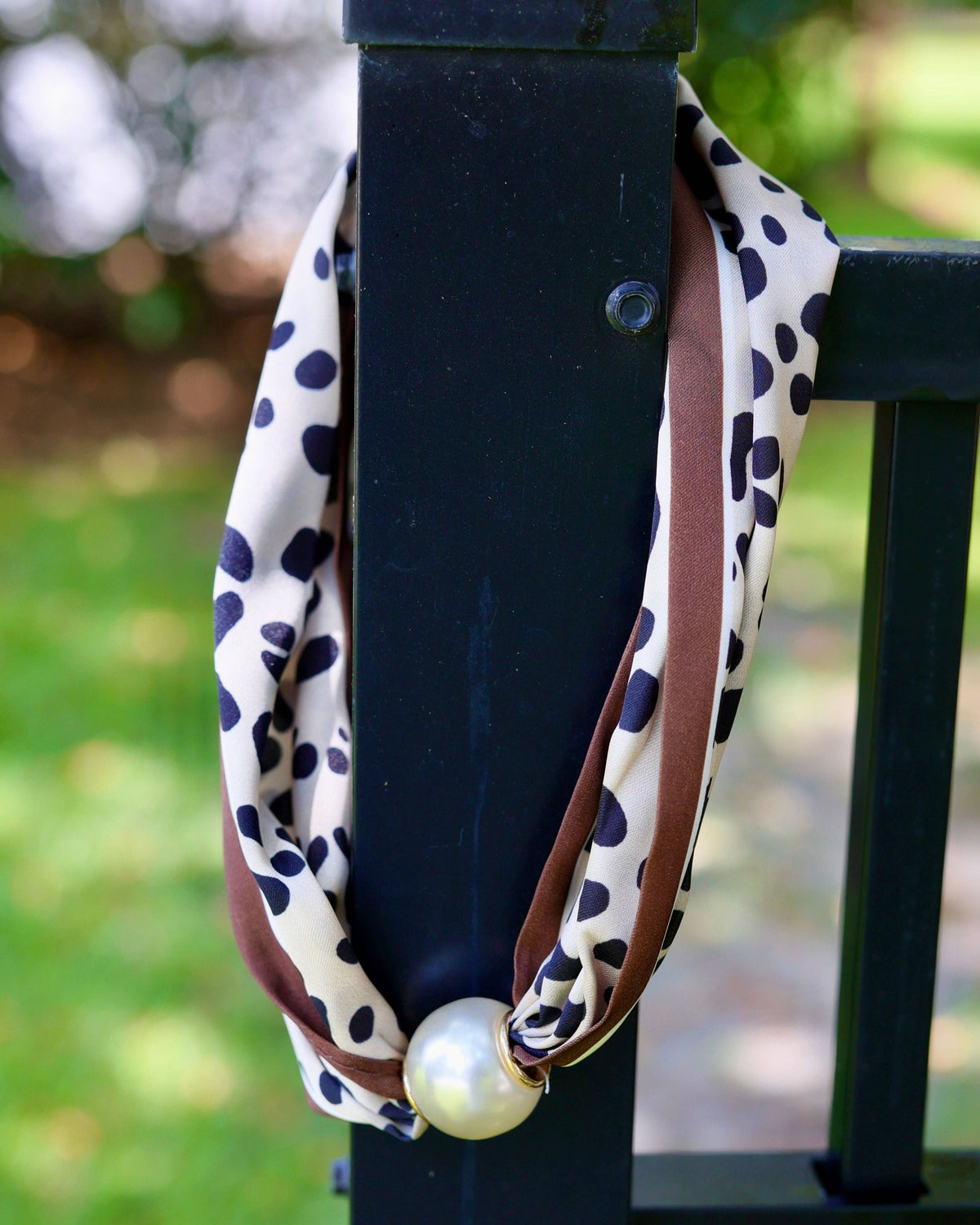 Cream leopard print scarf necklace with brown trim and magnetic pearl closure on fence