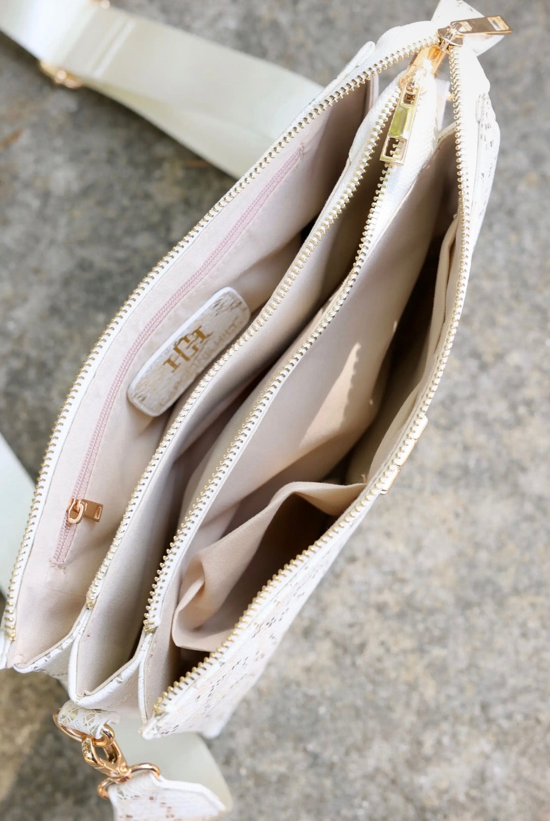 White crossbody purse interior showing gold zippers, multiple compartments, and brand tag