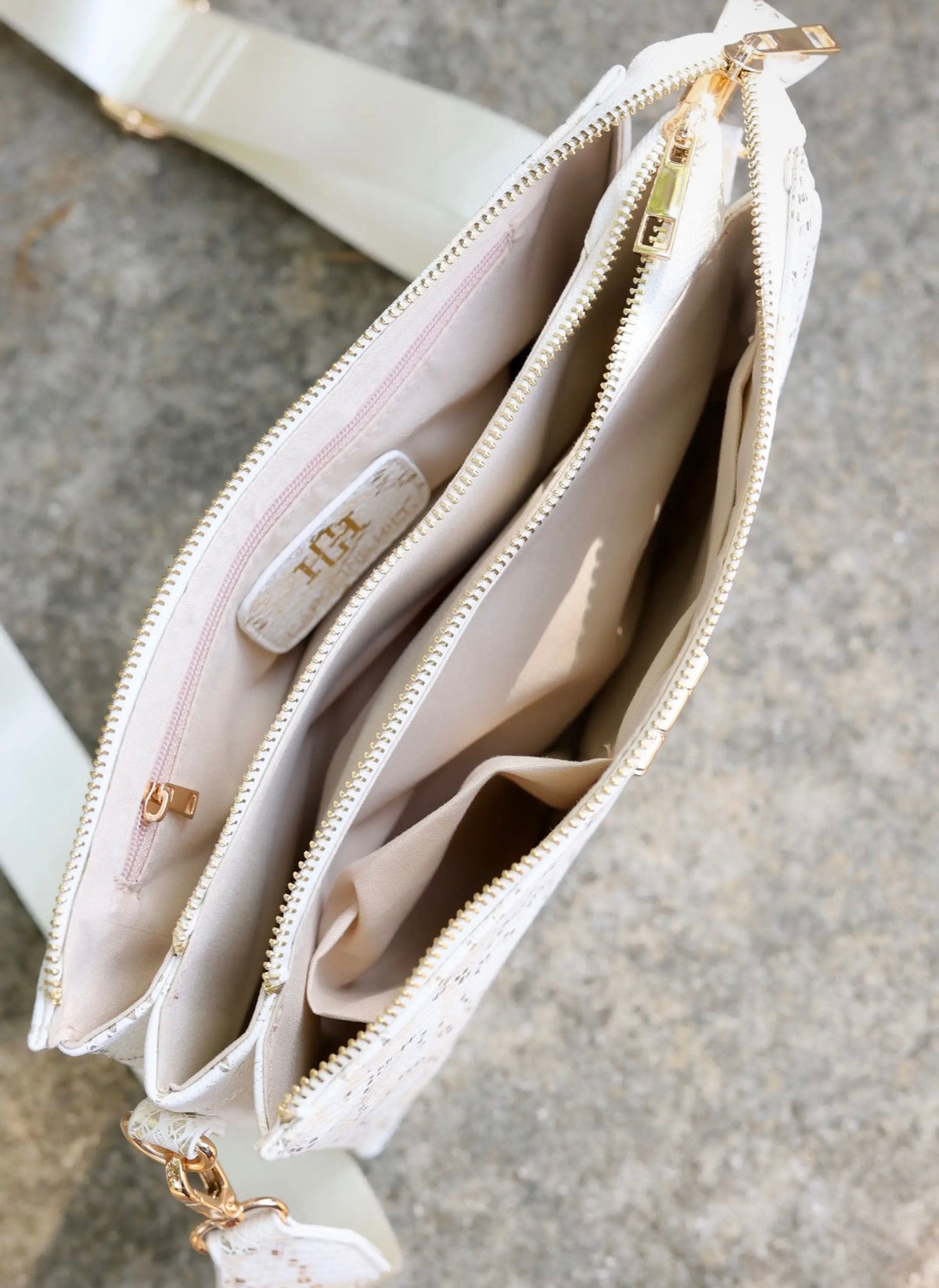White crossbody purse interior showing gold zippers, multiple compartments, and brand tag