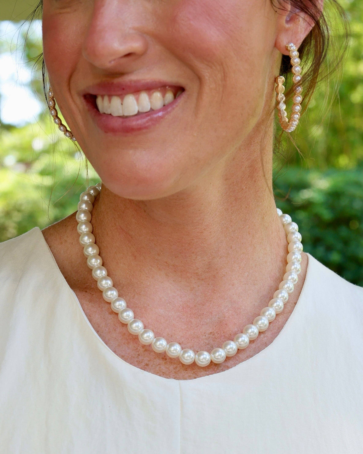Woman wearing classic white pearl strand necklace with matching pearl hoop earrings