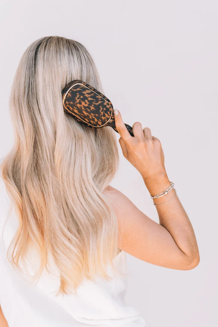 Woman brushing long blonde hair with tortoise shell paddle hair brush