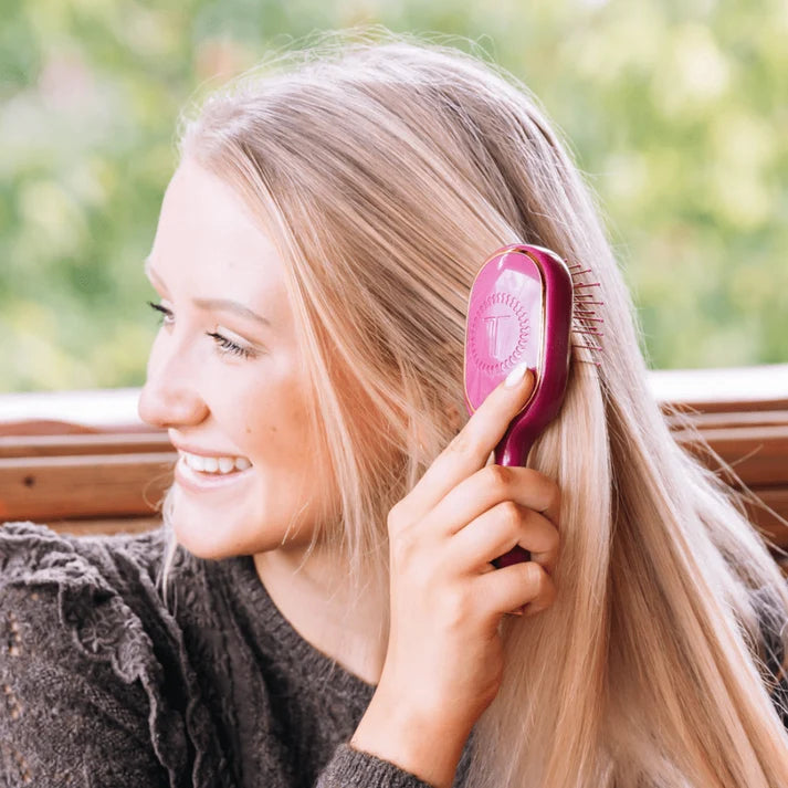 Woman brushing long blonde hair with mulberry pink TELETIES mini detangler brush