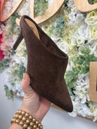 Corkys chocolate brown suede pointed-toe mule heels held against floral backdrop