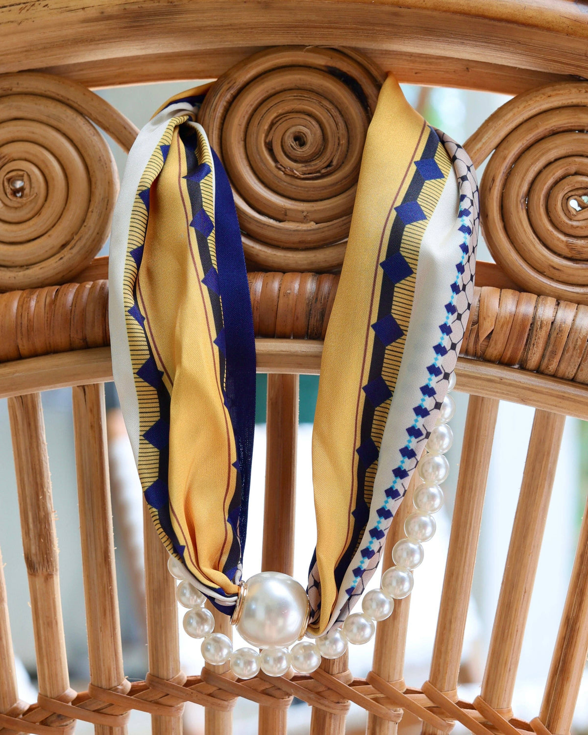 Two-strand pearl scarf necklace in navy and yellow geometric print on rattan chair