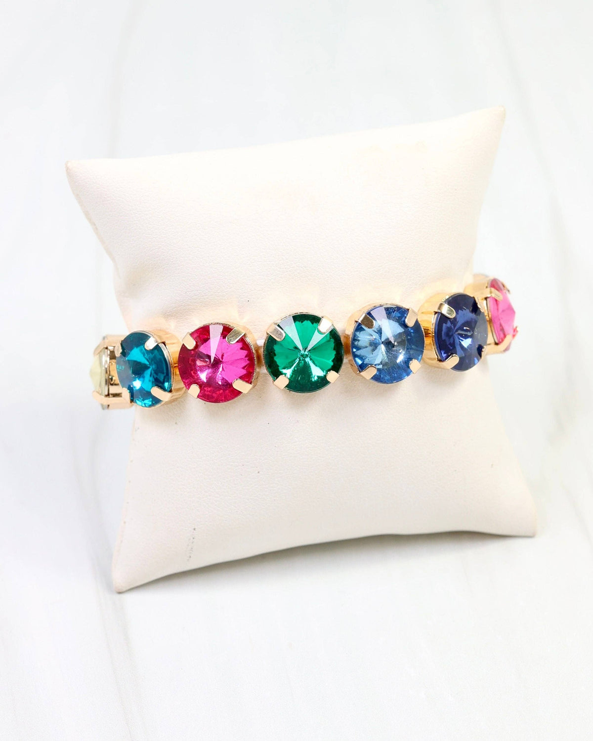 Multicolor rhinestone stretch bracelet with gold settings on a cream jewelry pillow