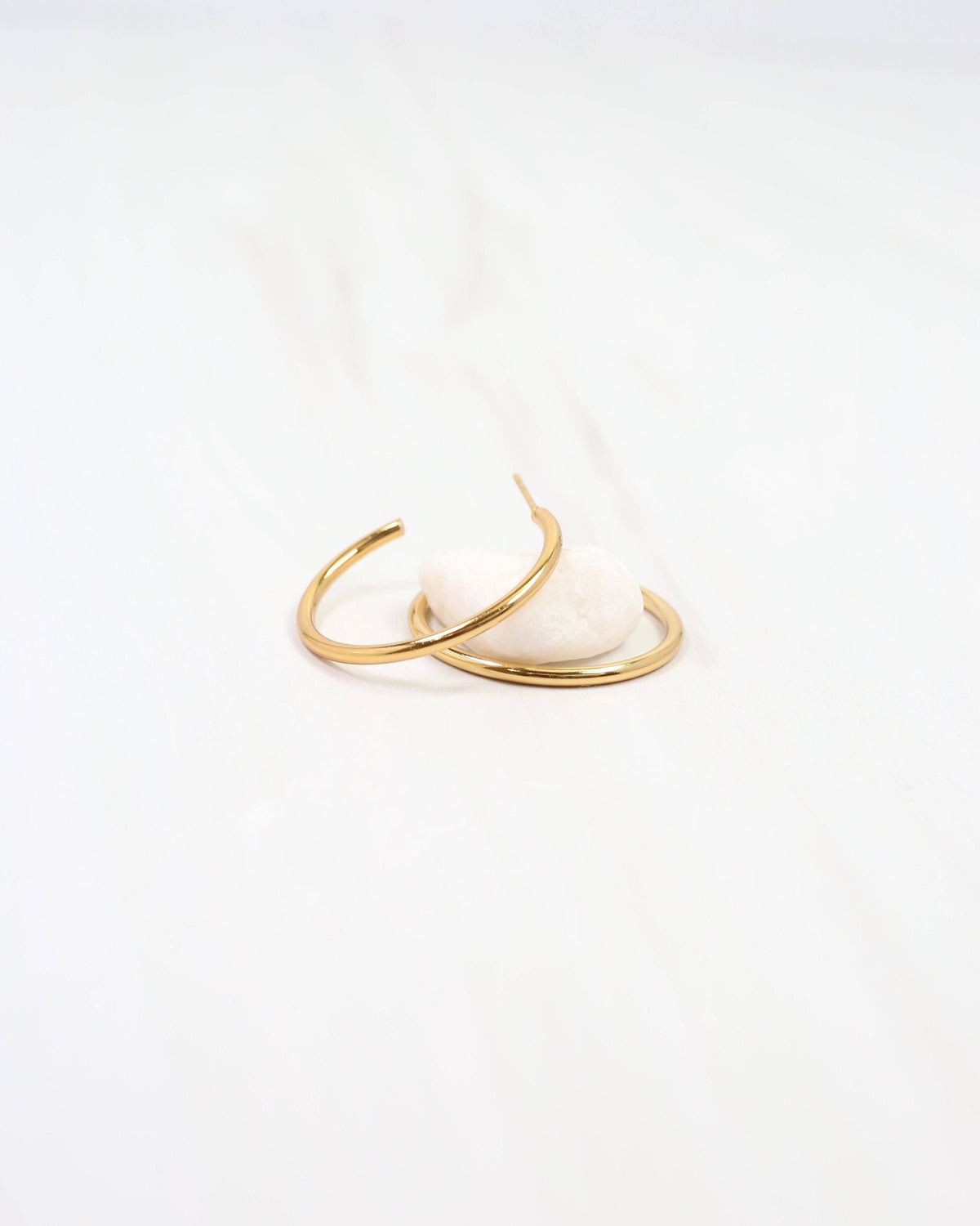 Caroline Hill Mayor thin gold hoop earrings displayed on a small white stone