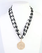 Black and white houndstooth skinny scarf worn as necklace with gold medallion pendant