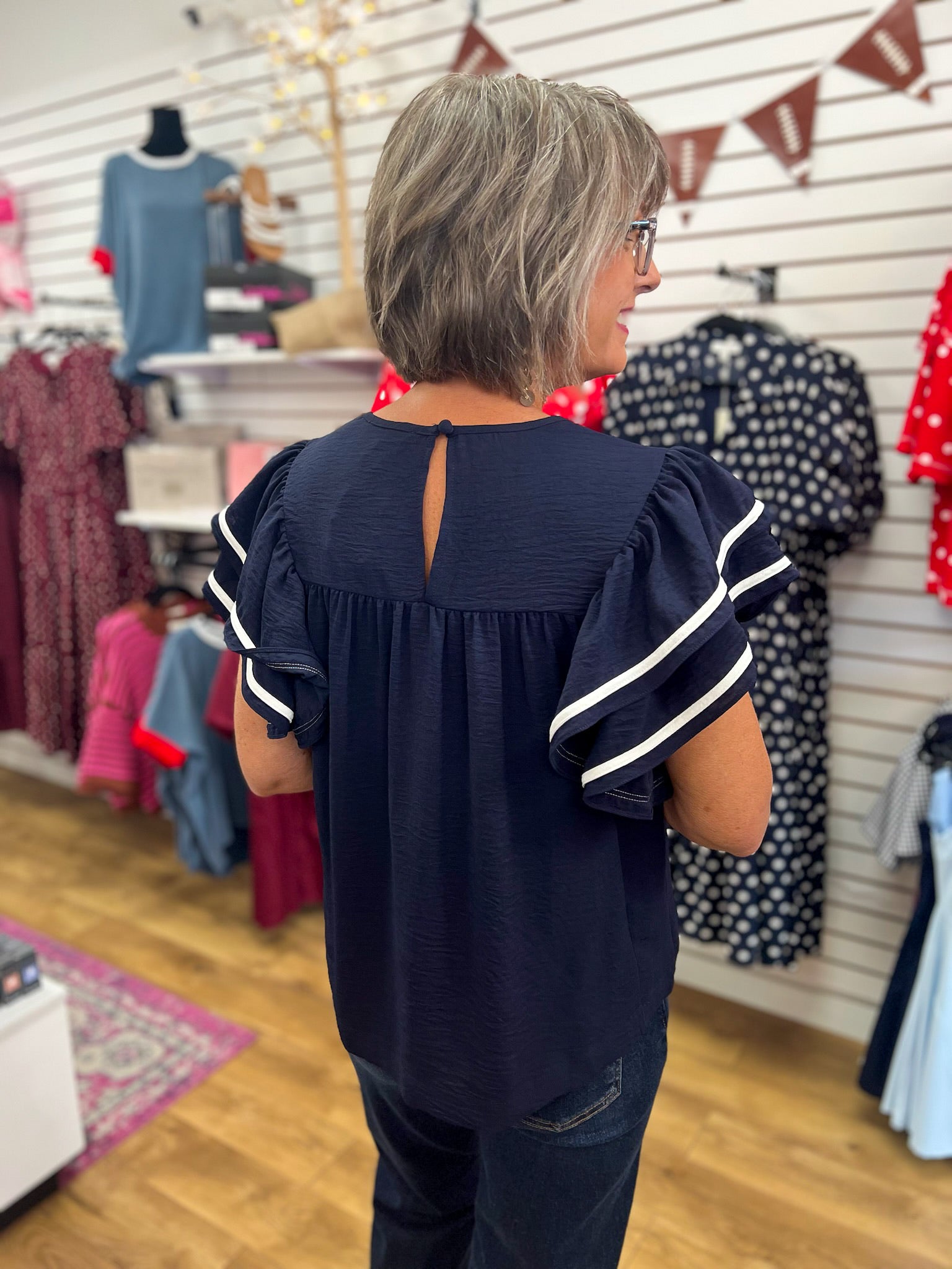 Navy blue ruffle sleeve top with white contrast piping, back view