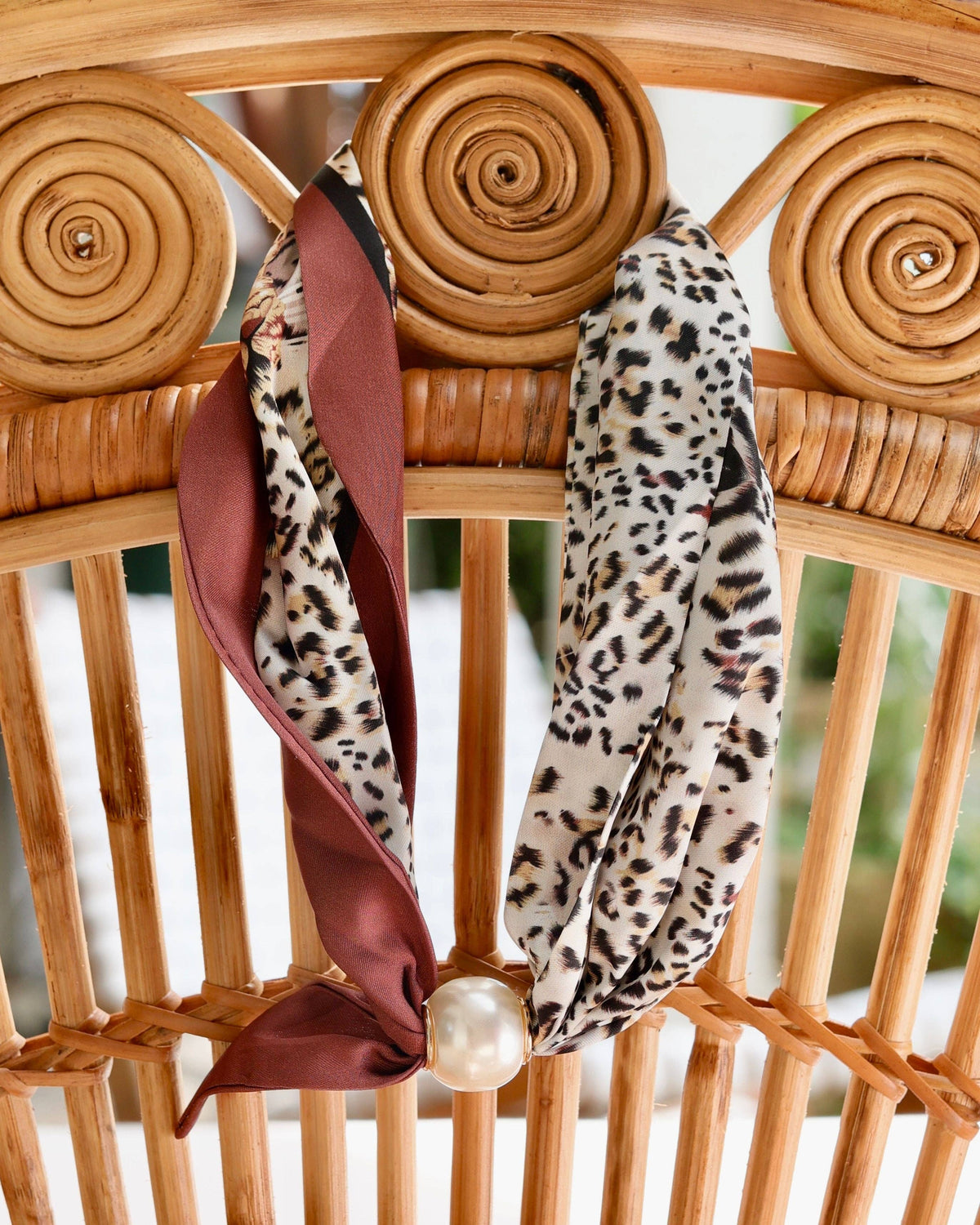 Leopard print scarf necklace with burgundy reverse and magnetic pearl closure on rattan chair