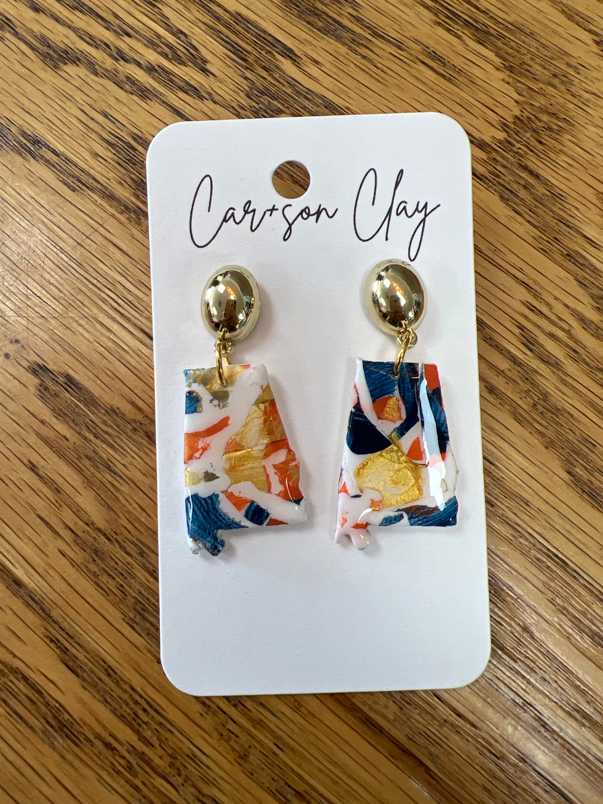 Clay drop earrings shaped like Alabama state in navy, orange, gold, and white swirl pattern