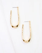 Gold hammered oblong hoop earrings with post backs on white marble surface