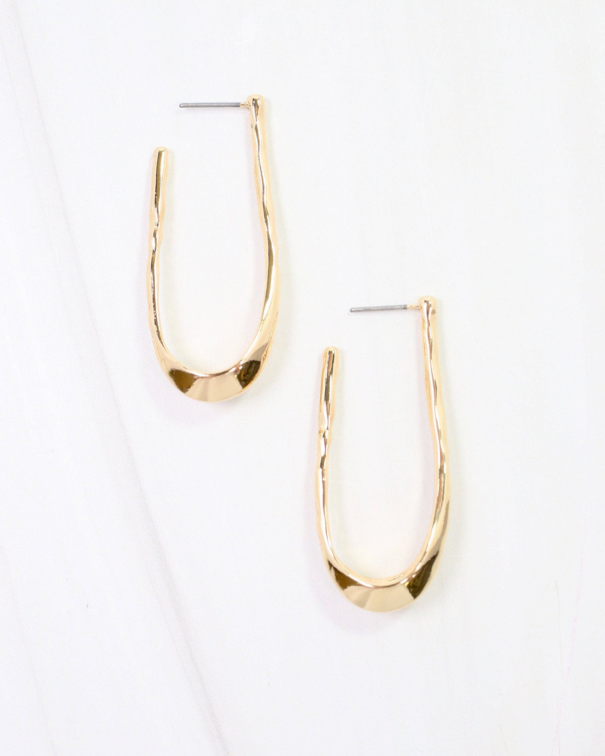 Gold hammered oblong hoop earrings with post backs on white marble surface
