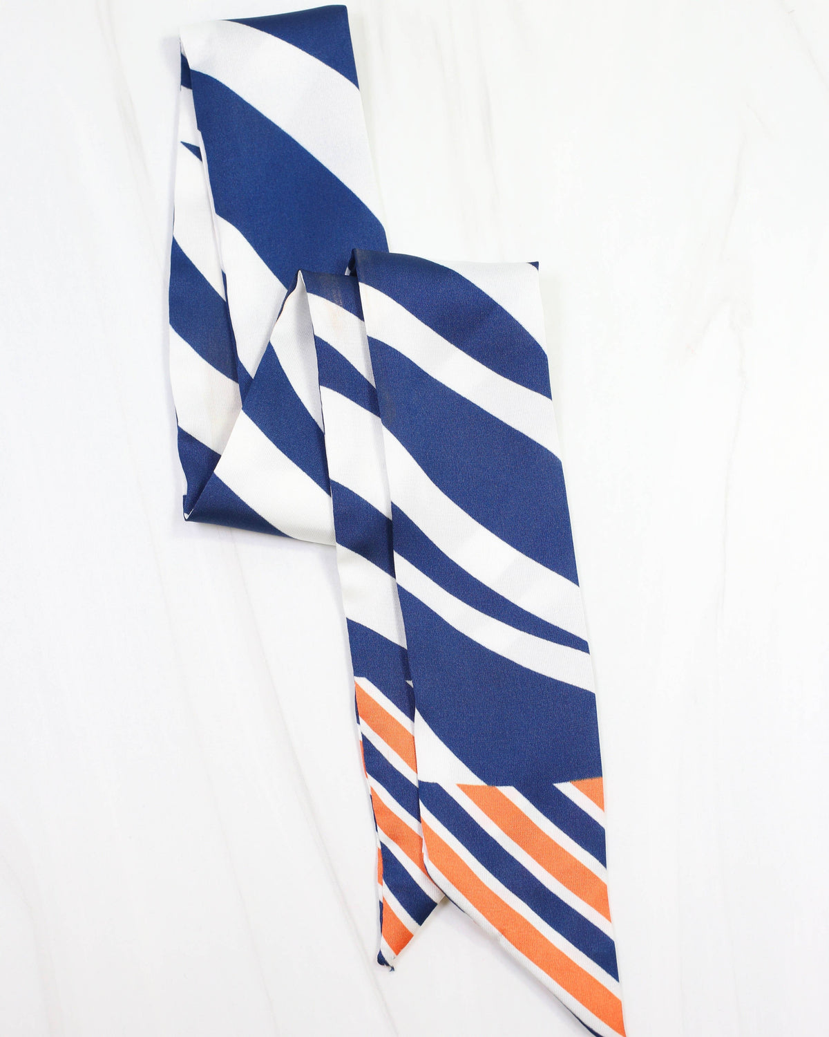 Navy blue white and orange diagonal striped skinny scarf laid flat