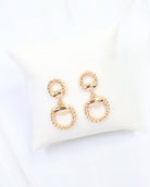 Gold braided horsebit drop earrings with twisted rope detail on ivory display pillow