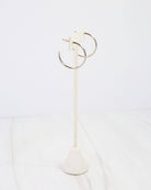 Silver thin hoop earrings displayed on a white marble earring stand