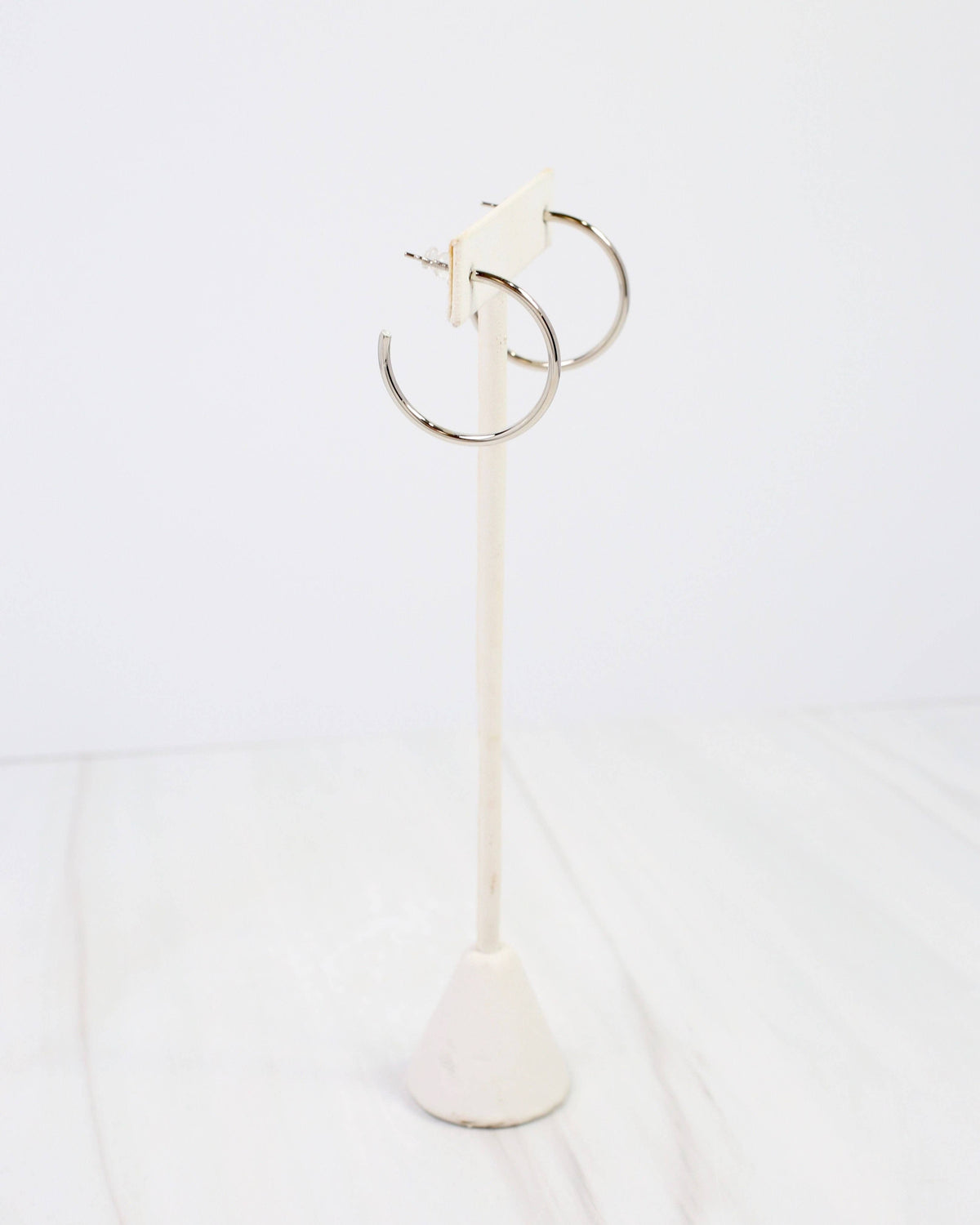Silver thin hoop earrings displayed on a white marble earring stand