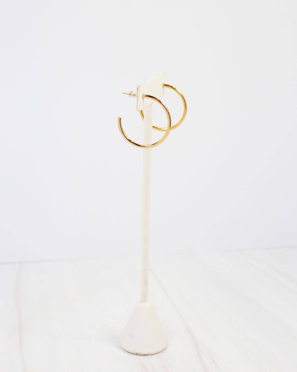 Gold thin open hoop earrings displayed on a white marble jewelry stand