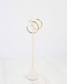 Gold thin open hoop earrings displayed on a white marble jewelry stand