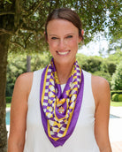 Purple and gold checkered silk scarf with floral accents worn around neck
