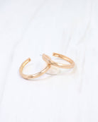 Hammered gold hoop earrings with open C-shape design on white marble surface