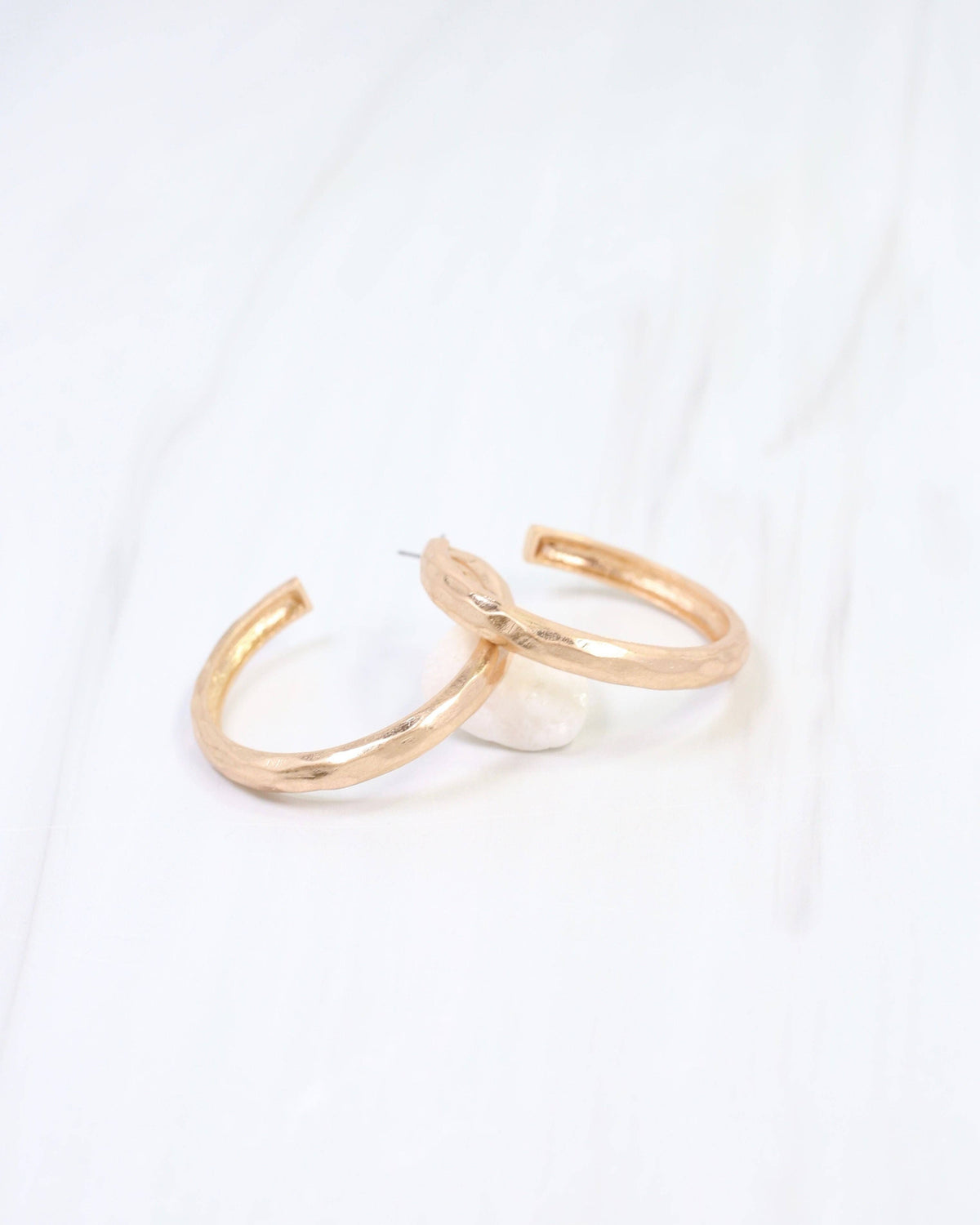 Hammered gold hoop earrings with open C-shape design on white marble surface