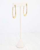 Gold oval hammered hoop earrings displayed on a white jewelry stand