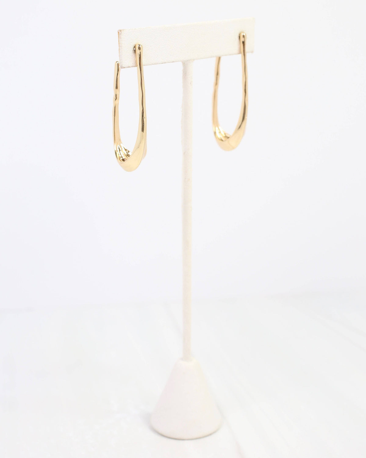 Gold oval hammered hoop earrings displayed on a white jewelry stand
