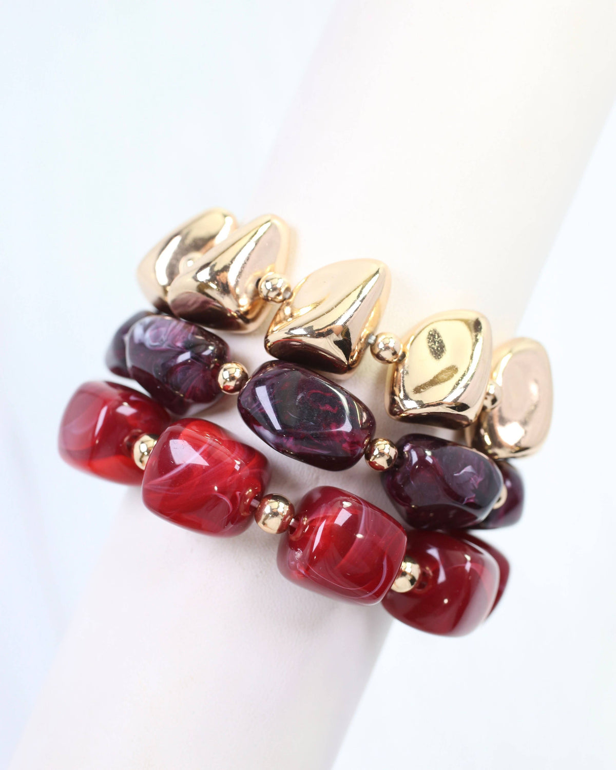 Stacked burgundy red and gold beaded stretch bracelet set on white display