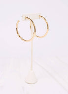 Caroline Hill Arden gold satin hoop earrings displayed on white earring stand