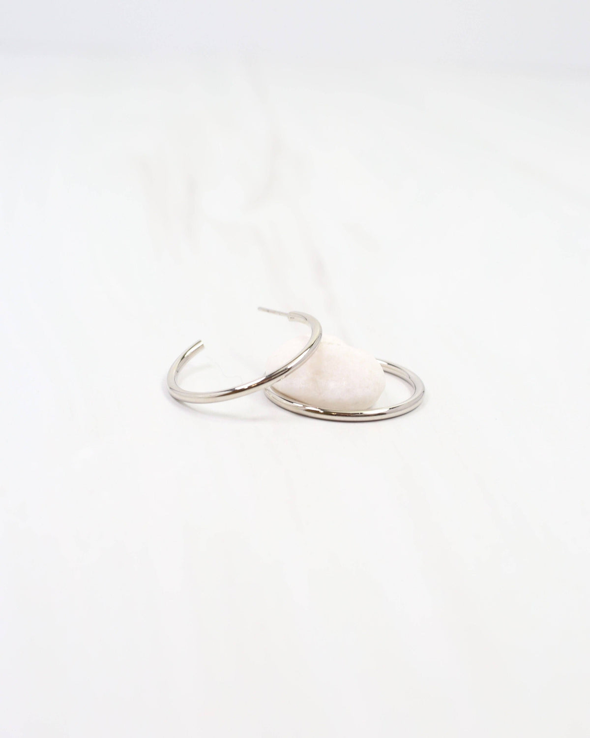 Caroline Hill Mayor thin silver hoop earrings displayed on white surface with stone prop